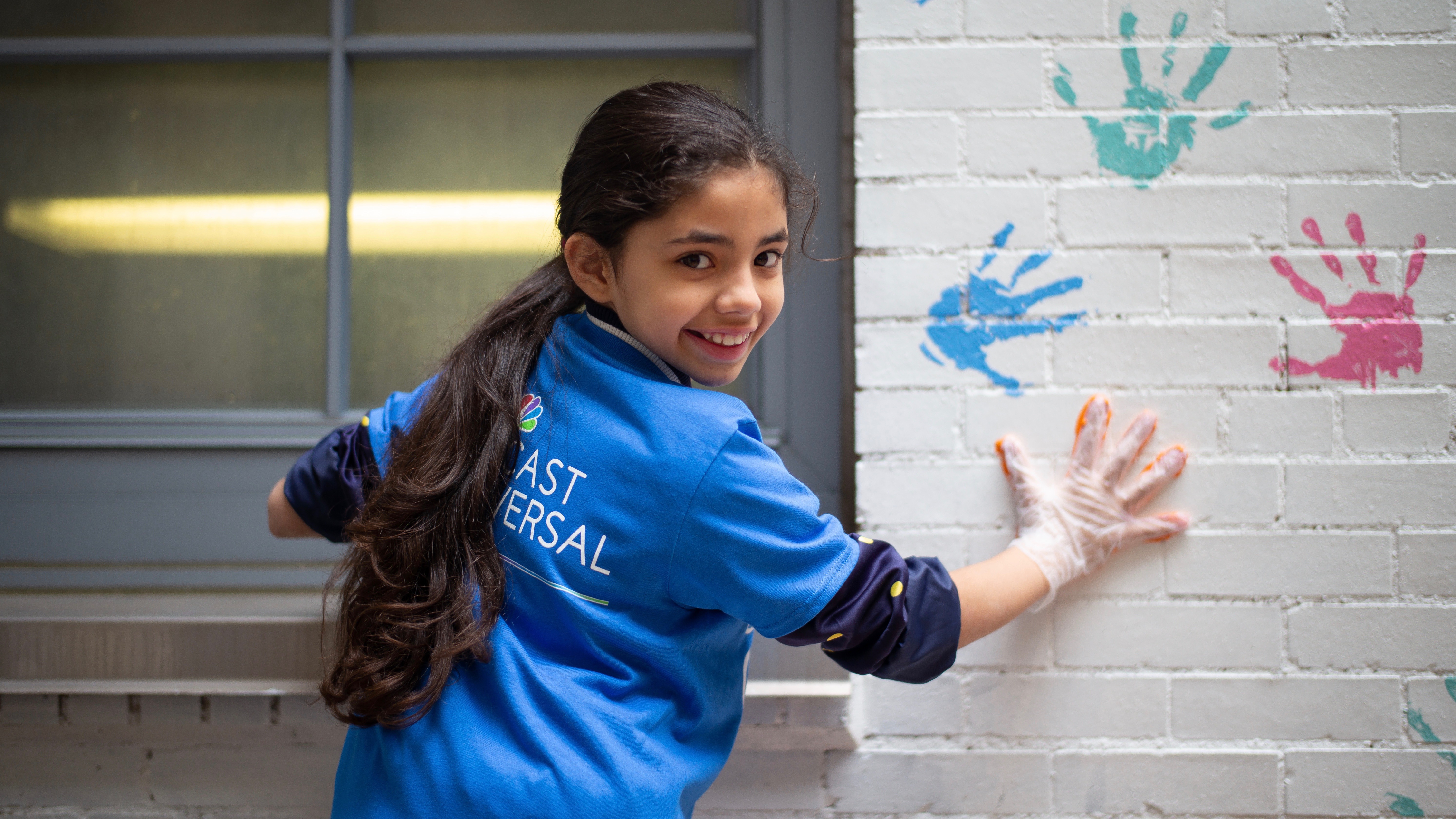 Little girl stamping her hand on a wall with paint